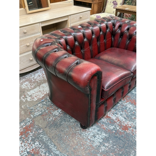 173 - An oxblood leather Chesterfield two-seater sofa - approx. 76cm high x 140cm wide x 75cm deep