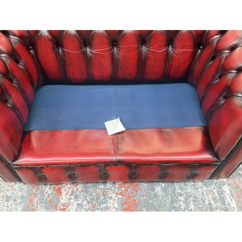 173 - An oxblood leather Chesterfield two-seater sofa - approx. 76cm high x 140cm wide x 75cm deep