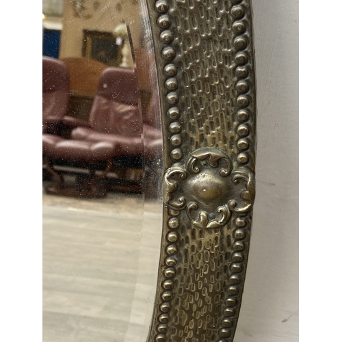 283 - An arts and crafts style embossed brass framed oval bevelled edge wall mirror - approx. 70cm high x ... 
