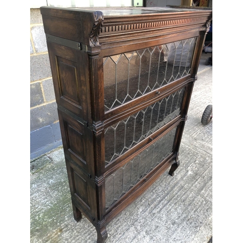 131 - An oak sectional bookcase, three sections each with leaded lift up and over glazed doors. 90cm x 31c... 