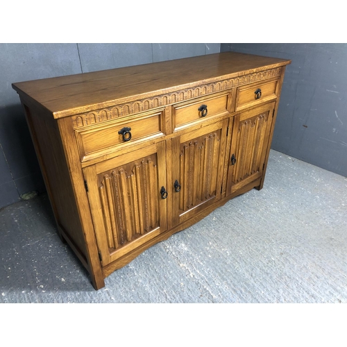 10 - A modern oak sideboard with three drawers over three cupboards, decorated with linenfold style decor... 