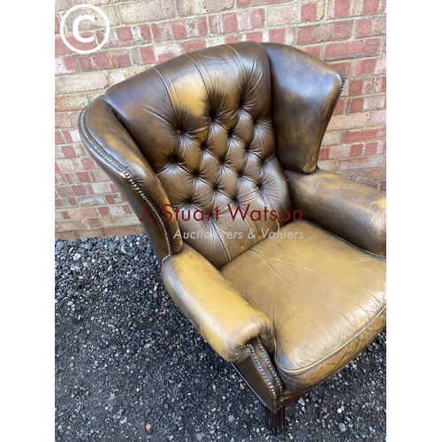 84 - A brown leather wing back Chesterfield armchair