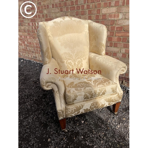 23 - A gold pattern upholstered wing back armchair raised on yew wood legs and brass castors