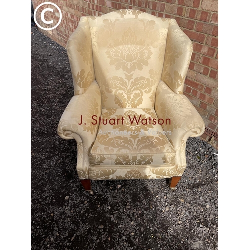 23 - A gold pattern upholstered wing back armchair raised on yew wood legs and brass castors