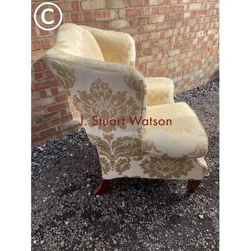 23 - A gold pattern upholstered wing back armchair raised on yew wood legs and brass castors