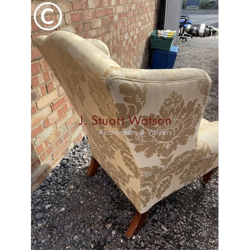 23 - A gold pattern upholstered wing back armchair raised on yew wood legs and brass castors