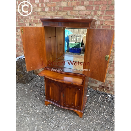 291 - A reproduction yew wood drinks cabinet with mirror glass interior and serving slide