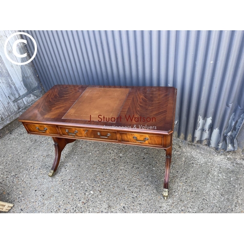 23 - A reproduction mahogany three drawer writing table with leather top