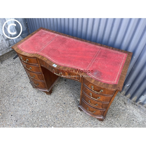 27 - A reproduction mahogany kneehole desk with serpentine front and red leather top