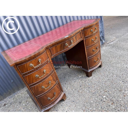 27 - A reproduction mahogany kneehole desk with serpentine front and red leather top