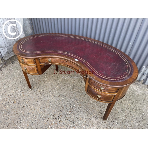 9 - A reproduction mahogany kidney shaped writing table with red leather top 148cm wide