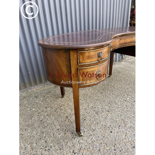 9 - A reproduction mahogany kidney shaped writing table with red leather top 148cm wide