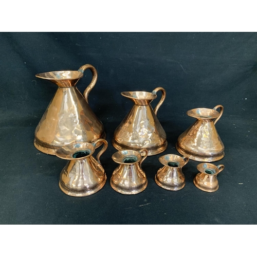 557 - Set of seven graduated copper measuring jugs