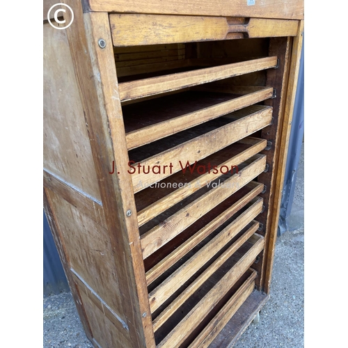 36 - An original vintage bakers 'bun cabinet' tambour front enclosing pine bun drawers. On large castors ... 