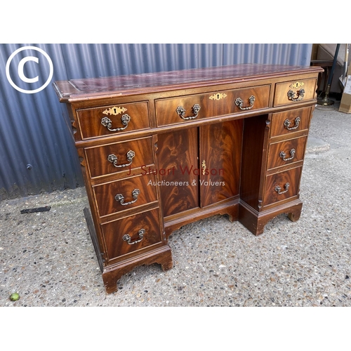 245 - A reproduction mahogany kneehole writing desk with a red leather top