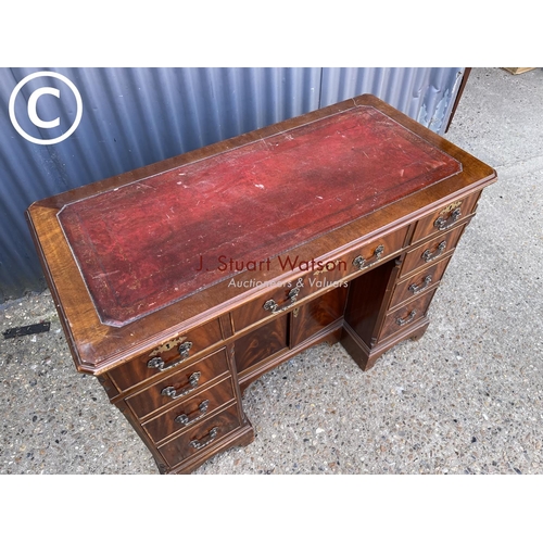 245 - A reproduction mahogany kneehole writing desk with a red leather top