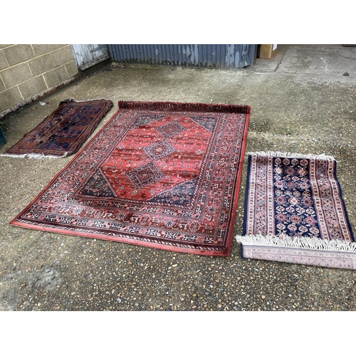 105 - A large modern red pattern rug together with two other oriental rugs