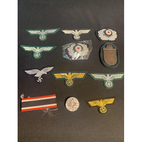 729 - A collection of 12 WW2 German retrospective metal and cloth copies of cap, breast and shoulder badge... 