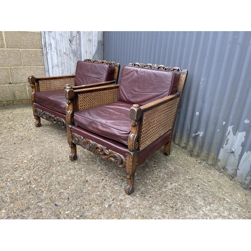 31 - A pair of early 20th century carved oak framed begere armchairs, upholstered in maroon leather