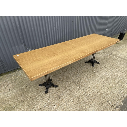 86 - A large light oak dining table with two ornate cast iron supports 82x240