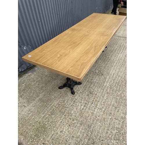 86 - A large light oak dining table with two ornate cast iron supports 82x240