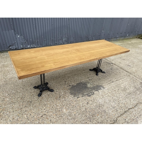 87 - A large light oak dining table with two ornate cast iron supports 82x241