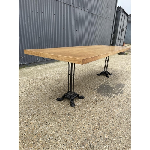 87 - A large light oak dining table with two ornate cast iron supports 82x241