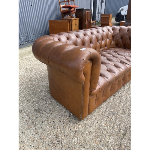 30 - A tan brown leather three seater chesterfield sofa with deep buttoned seat