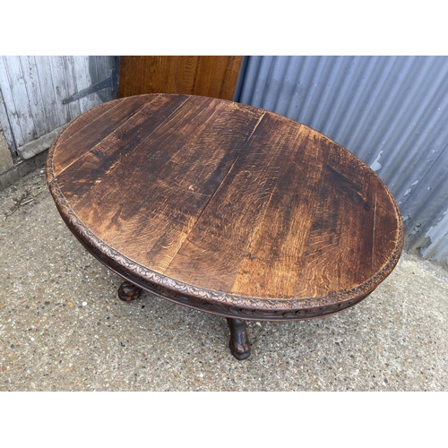 48 - A large oak oval dining table with pedestal base decorated with four carved  lions heads 127x110 plu... 