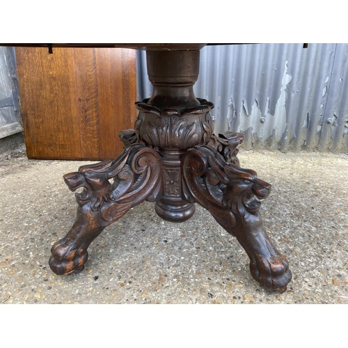 48 - A large oak oval dining table with pedestal base decorated with four carved  lions heads 127x110 plu... 