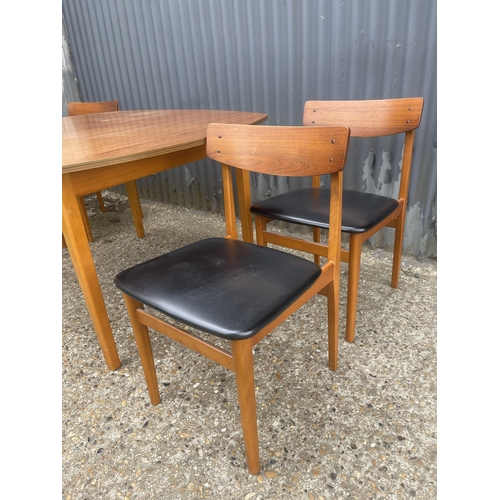 130 - An extending teak dining table together with four teak dining chairs with black vinyl seats