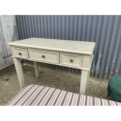 100 - A modern painted three drawer side table together with a green upholstered stool and a fabric ottoma... 