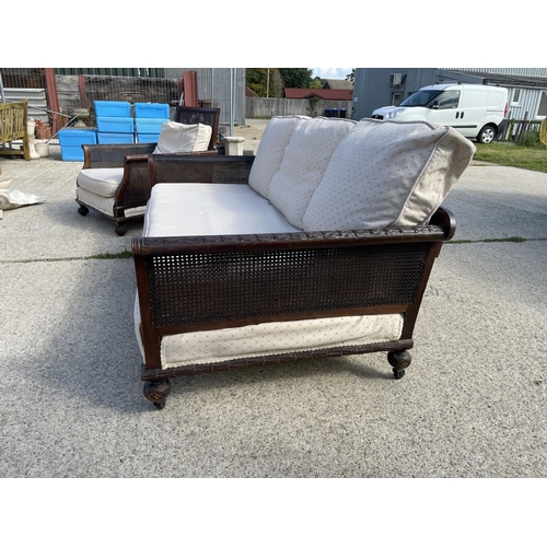 312 - An Edwardian mahogany framed begere sofa with matching armchair, loose cushions upholstered in cream... 