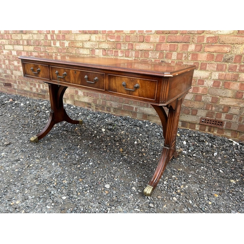 24 - A reproduction mahogany three drawer writing table with brown leather surface