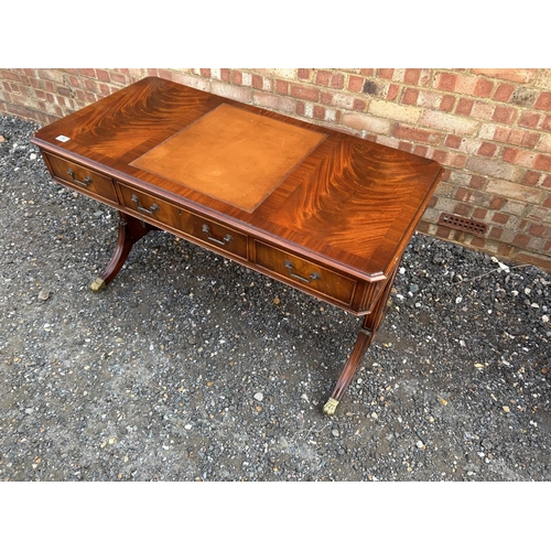 24 - A reproduction mahogany three drawer writing table with brown leather surface