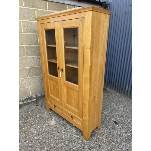 88 - A modern light oak two door glazed cabinet with two drawers 107x35x170