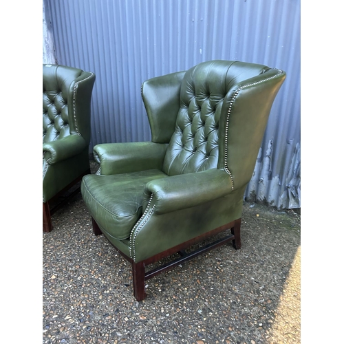 350a - A pair of green leather chesterfield wing back armchairs