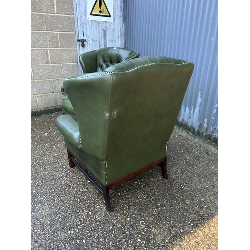 350a - A pair of green leather chesterfield wing back armchairs