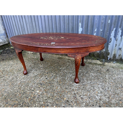 153 - An eastern rosewood oval coffee table with brass inlay
