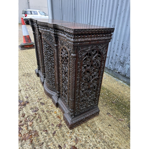 243 - An antique Burmese hardwood side cabinet, ornately carved 132x38x97 cms