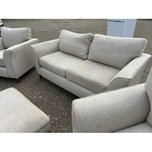 253 - A beige upholstered four piece lounge suite consisting of two seater sofa, two chairs and a footstoo... 