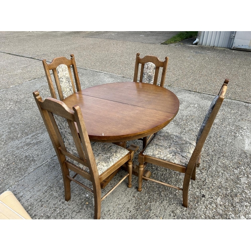 194 - A circular oak dining table with four chairs and extension leaf