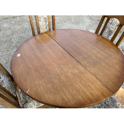 194 - A circular oak dining table with four chairs and extension leaf