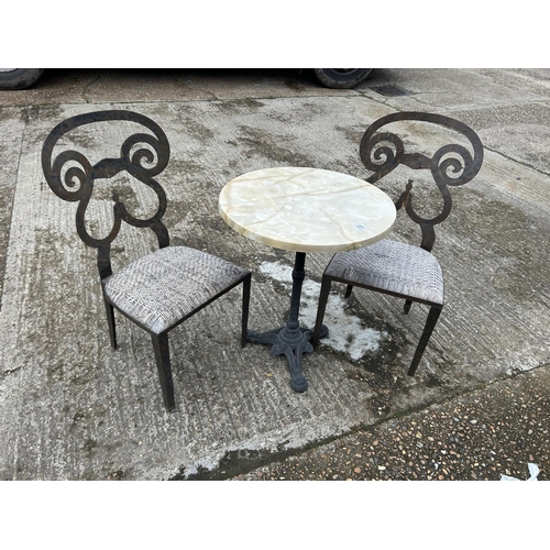 176 - A circular iron framed bistro table with marble top and two iron framed chairs