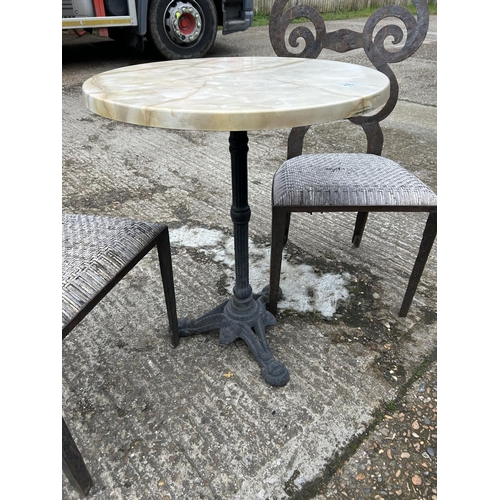 176 - A circular iron framed bistro table with marble top and two iron framed chairs