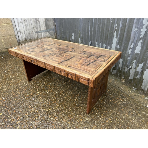 86 - A carved hardwood ethnic style coffee table with drop in glass top 107x56x47