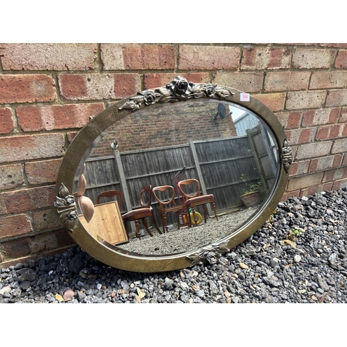 364 - A arts and crafts style planished brass oval wall mirror decorated with roses  85x60