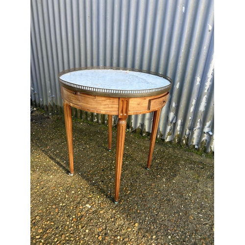 215 - A continental circular mahogany table with a white marble top and brass gallery. Fitted with two dra... 