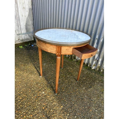 215 - A continental circular mahogany table with a white marble top and brass gallery. Fitted with two dra... 