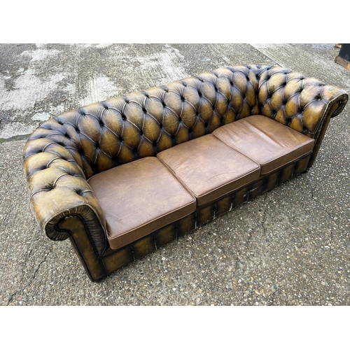 63 - A golden brown leather chesterfield three seater sofa